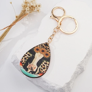 Detail of teardrop keychain with cow and sunflower print on rustic white display