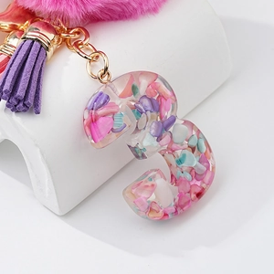 Détail du porte-clés lettre 3 en résine avec pierres colorées, pompon rose et gland violet