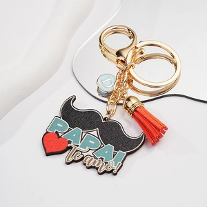 Close-up of mustache keychain with Papai te amo text, orange tassel, and blue D charm