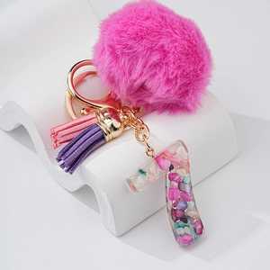 Détail du pendentif chiffre 7 en résine avec pompon rose et glands sur présentoir blanc