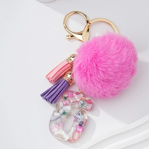 Détail de pompon en fausse fourrure rose, glands et pendentif lettre G en résine sur porte-clés