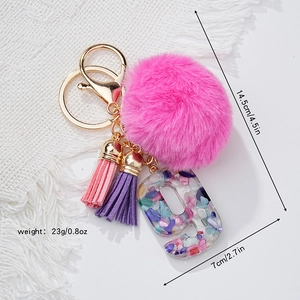 Dettaglio pompon in pelliccia rosa e nappa viola con portachiavi lettera g in resina