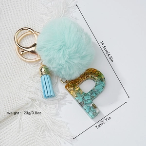 Détail de la lettre P en résine avec feuille d'or, pompon vert et frange bleue sur porte-clés