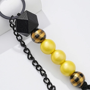 Close-up of beaded keychain featuring a dark wood polyhedron and yellow matte round beads