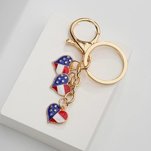 Golden keychain with three heart pendants featuring American flag patterns on a white stand
