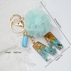 Détail du porte-clés lettre M en résine avec feuille d'or, turquoise et pompon bleu