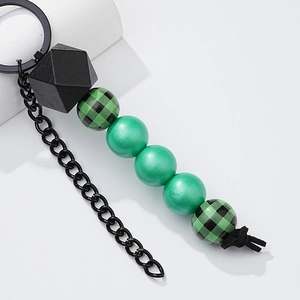 Detail of wooden beaded keychain with green plaid and geometric black beads on white surface