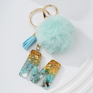 Porte-clés lettre M en résine turquoise et feuille d'or avec pompon et gland vert