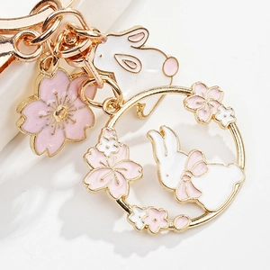Detailed close-up of pink cherry blossom and white rabbit enamel pendant on a golden keyring