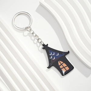 Detailed view of haunted house keychain with bats and glowing window on white stand