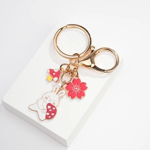 Detail of golden keychain with white bunny, pink flower and red mushroom charms