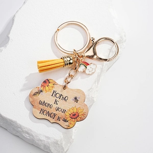 Detail of wooden sunflower keychain with yellow tassel and rainbow charm on stone
