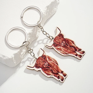 Detail view of two creative highland cow wooden keychains on a white natural stone