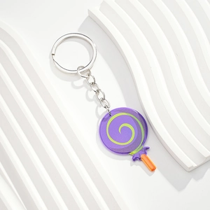 Detailed close-up of a purple lollipop keychain with green swirls on white wavy background