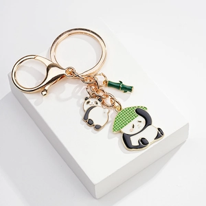 Detail of golden panda keychain with green hat charm and bamboo pendant on white stand