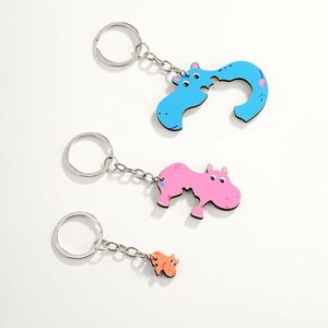 Three wooden cartoon hippo keychains in blue, pink, and orange showing size variations