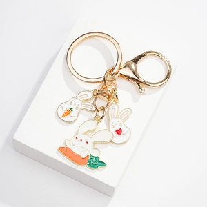Detailed close-up of cute white enamel bunny charms and carrot pendant on gold keychain