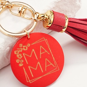 Red leather tassel keychain with golden MAMA engraved round pendant on marble background