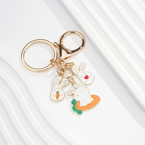 Detail of gold metal keychain with white enamel rabbit charms and carrot accents