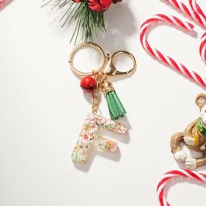 Detail of Christmas resin letter F keychain with red bell and green tassel on white background