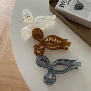 Three elegant bow hair claws in cream, amber, and grey colors shown on a stylish white desk