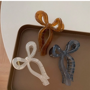 Detail view of large bow hair claws in amber, cream, and smoky grey on a tray