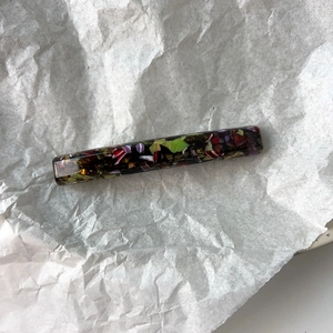 Close-up of floral mosaic acetate hair clip texture on a minimalist white paper background