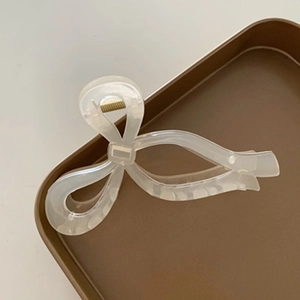 Detail of elegant white bow hair claw clip showing translucent texture and gold metal spring