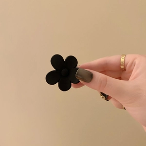 Handbeeld van een matzwarte bloem haarklem met minimalistische acryl afwerking in zwart