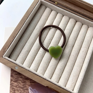 Détail d'un pendentif cœur vert avec lettrage doré sur un élastique à cheveux marron