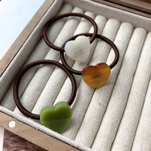 Gros plan d'élastiques à cheveux cœur en ivoire, ambre et vert matcha dans une boîte à bijoux