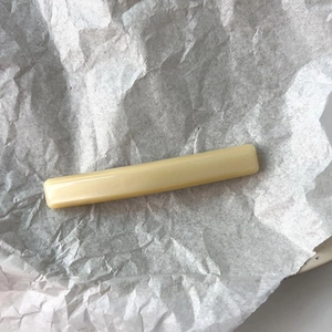 Minimalist cream yellow rectangular resin hair clip on a textured white paper background