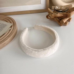 Gros plan d'un serre-tête épais en peluche blanc crème avec texture douce sur plateau bois