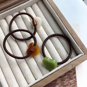 Trois élastiques à cheveux avec pendentifs cœur en crème, ambre et vert dans une boîte