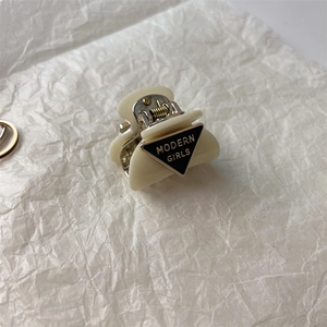 Close-up of cream resin mini hair claw clip featuring Modern Girls typography on black accent