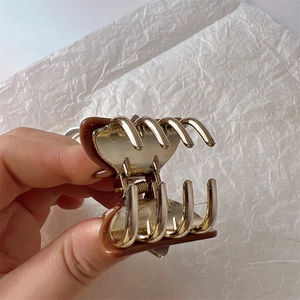 Detailed close-up of dark brown acrylic shark hair claw with gold metal prongs