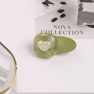 Détail d'une pince à cheveux vert marbré avec un cœur blanc dans un décor minimaliste