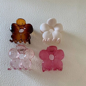 Detail of four colorful resin camellia flower hair claws in pink, cream, and amber tones