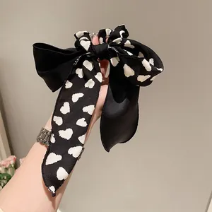 Detailansicht des schwarzen Satin-Haargummis mit weißen Herzen und langen fließenden Bändern