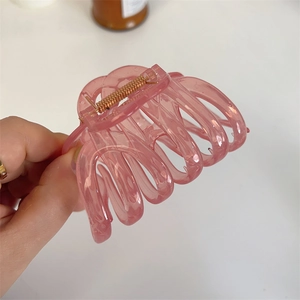 Detail of a pink translucent hair claw clip with cross-braided design and strong metal spring