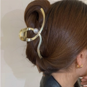 Detailed view of a gold wavy hair claw clip featuring a single pearl on a woman's hair