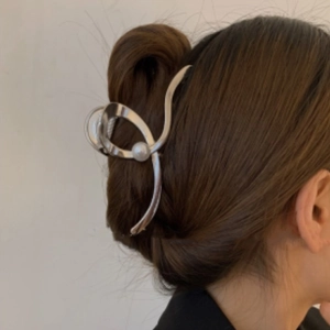 Detail view of large silver metal hair claw clip with pearl on woman's brown hair
