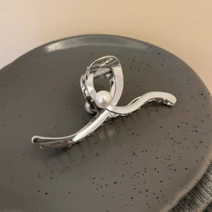 Detail of silver metal hair claw with pearl accent on a grey decorative tray