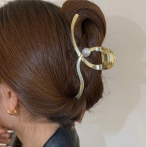Minimalist gold metal hair claw with pearl accent worn on a model's hair