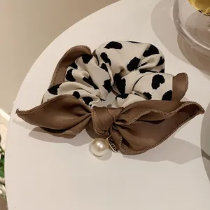 Detailaufnahme von Haargummi mit Kuhmuster, brauner Schleife und elegantem Perlenanhänger