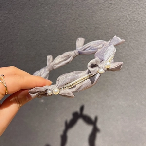 Détail d'un serre-tête en soie lavande avec nœud, perles blanches et strass brillants