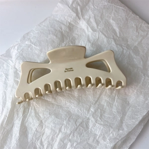 Detail of a large cream acetate hair claw clip with cutout design on white crinkle paper