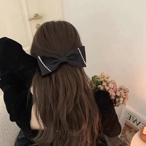 Detail of elegant black satin bow hair clip with pearl trim worn on the back of head