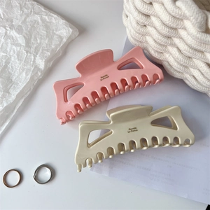 Detailed close-up of large acetate bow hair claws in pink and cream with French lettering