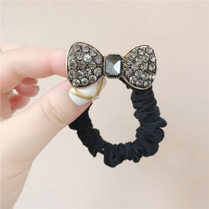 Detail view of black scrunchie with a vintage gold-edged bow and grey rhinestones